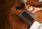 Top view male hands holding cup of coffee man sitting at round table in a cafe working on laptop had his smartphone and notebook drinking cappuccino